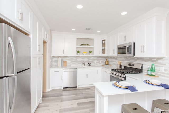 kitchen featuring stainless steel appliances, white cabinetry, sink, tasteful backsplash, and light hardwood / wood-style flooring