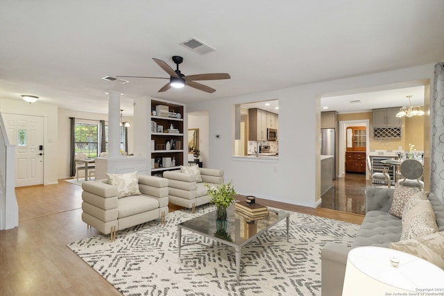 living room with ornate columns, light hardwood / wood-style floors, and ceiling fan with notable chandelier