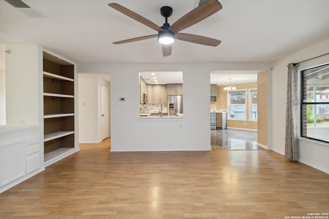 unfurnished living room with built in shelves, light wood-type flooring, and ceiling fan with notable chandelier