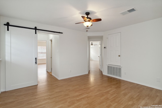 empty room with a barn door, light hardwood / wood-style floors, and ceiling fan