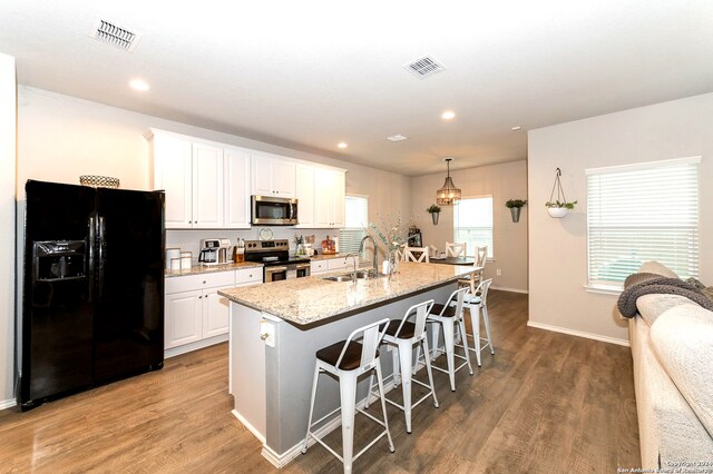 kitchen featuring a center island with sink, white cabinetry, appliances with stainless steel finishes, hardwood / wood-style floors, and sink