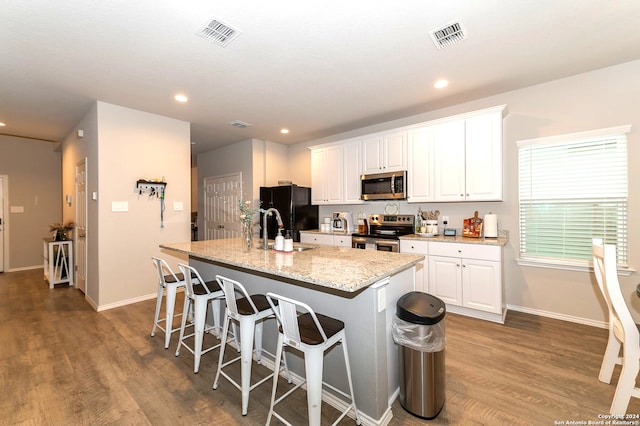 kitchen with dark wood-type flooring, appliances with stainless steel finishes, a kitchen island with sink, and white cabinets