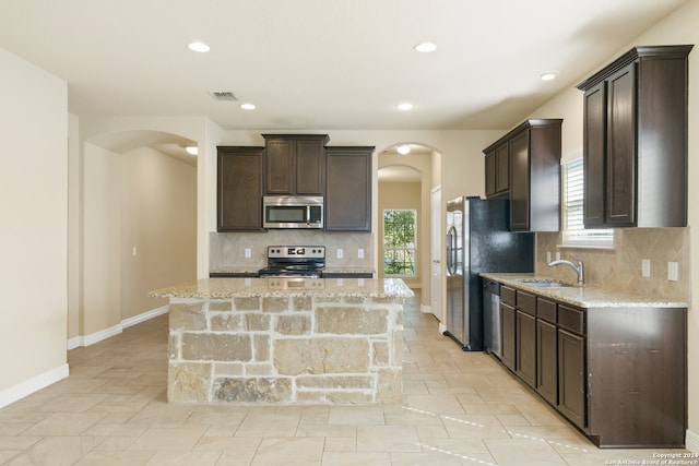 kitchen featuring tasteful backsplash, light stone counters, a kitchen island, and stainless steel appliances