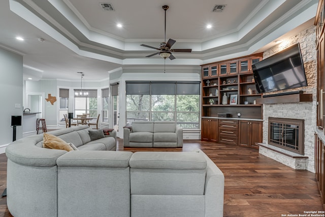 living room featuring ornamental molding, a fireplace, dark hardwood / wood-style floors, a raised ceiling, and ceiling fan with notable chandelier