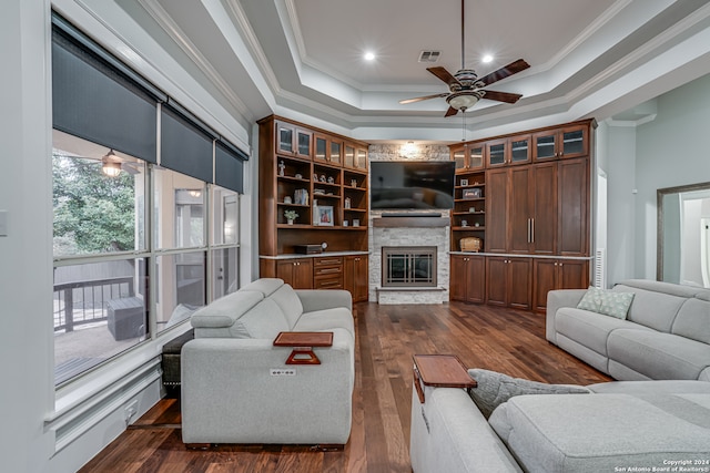 living room with dark hardwood / wood-style floors, a raised ceiling, a stone fireplace, and crown molding