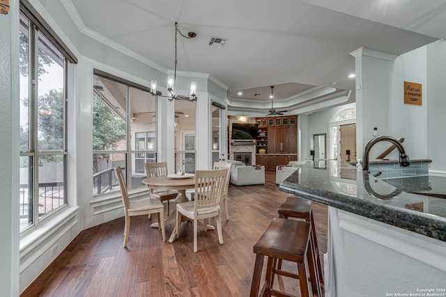 dining room with ornamental molding, a fireplace, dark hardwood / wood-style floors, a raised ceiling, and ceiling fan with notable chandelier