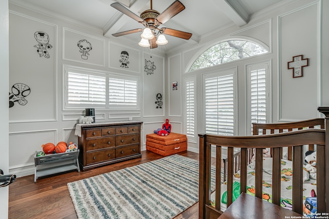 bedroom featuring a nursery area, ornamental molding, dark wood-type flooring, beamed ceiling, and ceiling fan