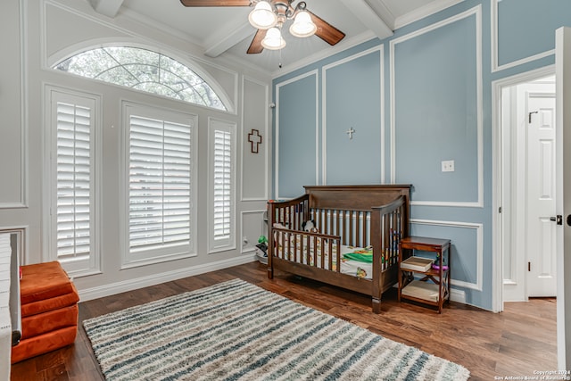 bedroom featuring ornamental molding, ceiling fan, beam ceiling, a crib, and wood-type flooring