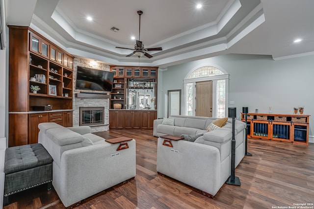 living room with dark wood-type flooring, ceiling fan, a raised ceiling, and crown molding