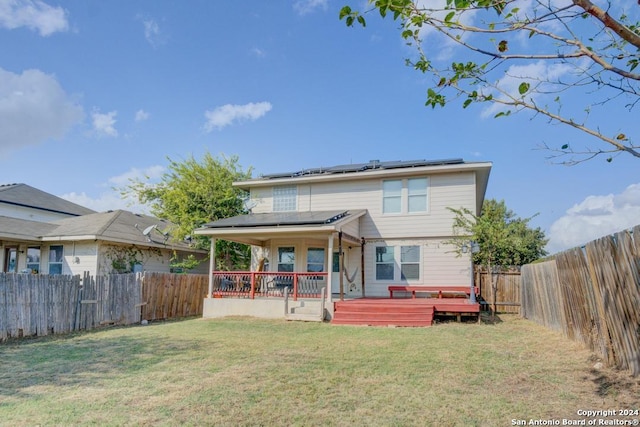 back of house with solar panels, a porch, a deck, and a lawn