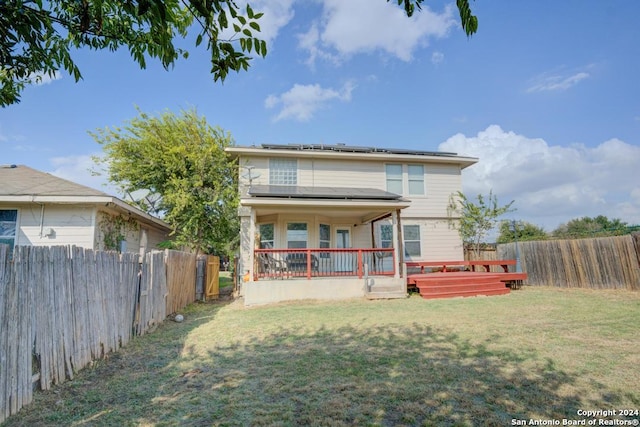 back of property with a yard, a deck, and solar panels