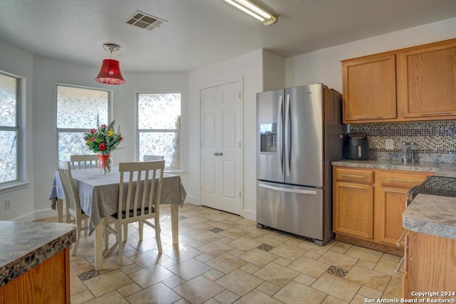 kitchen with pendant lighting, a textured ceiling, stainless steel refrigerator with ice dispenser, and tasteful backsplash