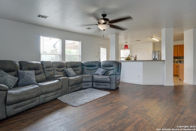 living room with a textured ceiling, ceiling fan, and dark wood-type flooring