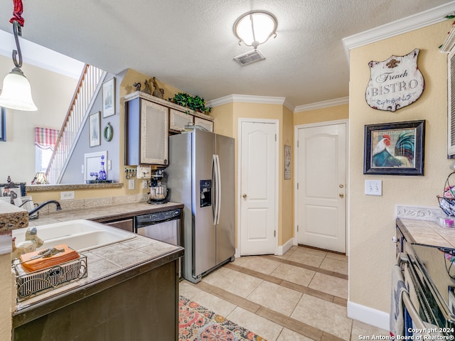 kitchen featuring tile countertops, hanging light fixtures, sink, ornamental molding, and appliances with stainless steel finishes