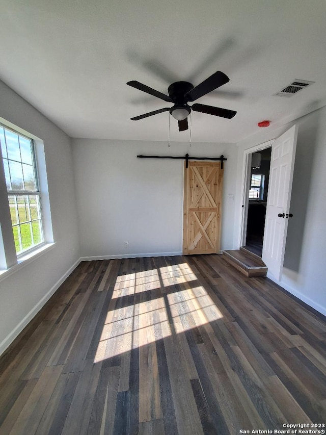 unfurnished room featuring a barn door, ceiling fan, and dark hardwood / wood-style flooring