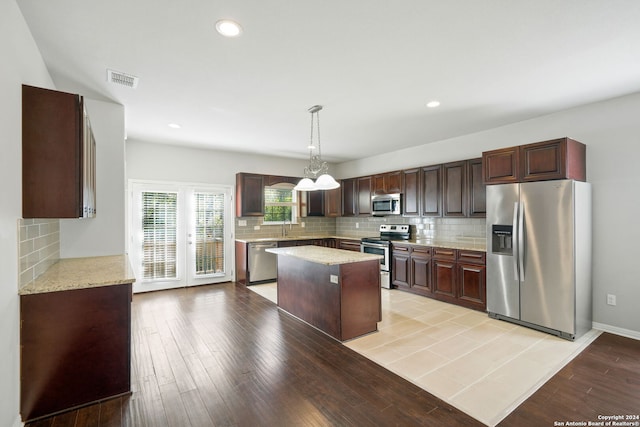 kitchen with a center island, decorative backsplash, pendant lighting, light wood-type flooring, and appliances with stainless steel finishes