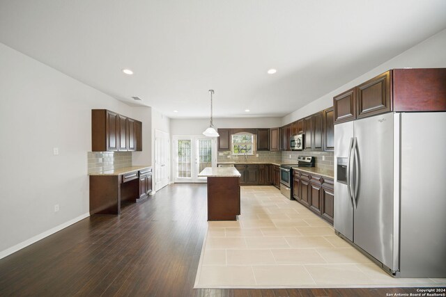 kitchen with a kitchen island, light wood-type flooring, appliances with stainless steel finishes, dark brown cabinets, and pendant lighting