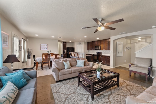 living room with light hardwood / wood-style floors, ceiling fan, and a textured ceiling