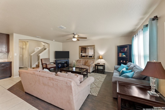 living room with dark wood-type flooring, ceiling fan, and a textured ceiling