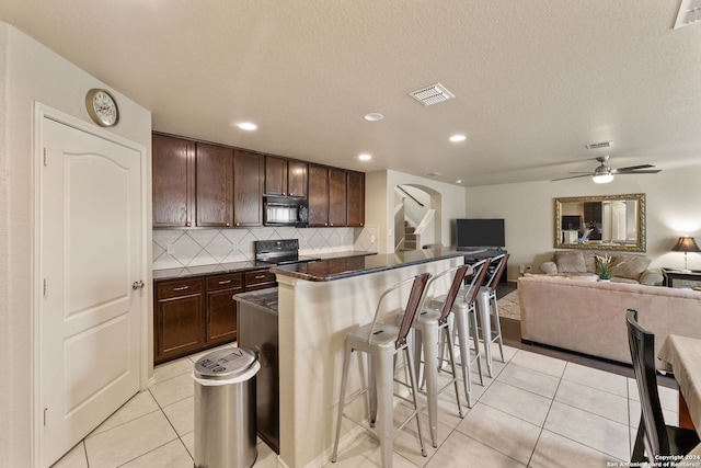 kitchen with black appliances, ceiling fan, a breakfast bar area, backsplash, and a center island