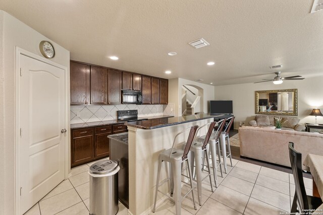 3922 Verde Bosque, San Antonio, TX 78223 - kitchen with black appliances, a breakfast bar, tasteful backsplash, light tile patterned floors, and dark brown cabinetry