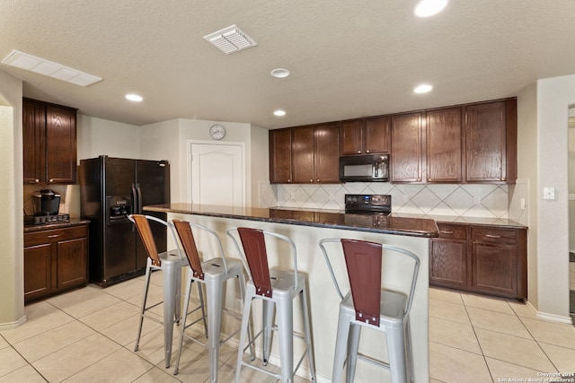 kitchen featuring a breakfast bar area, light tile patterned floors, black appliances, and tasteful backsplash