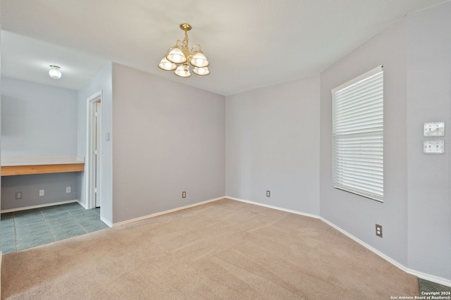 carpeted empty room featuring a chandelier and baseboards