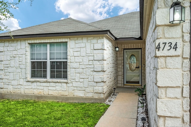entrance to property with stone siding and a shingled roof