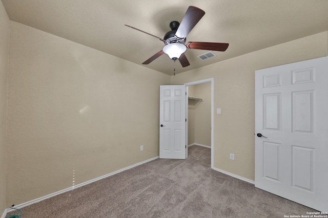 unfurnished bedroom featuring a walk in closet, ceiling fan, a closet, and light colored carpet