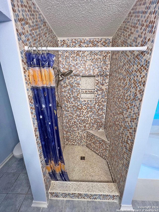 bathroom featuring tile patterned flooring, tiled shower, a textured ceiling, and toilet