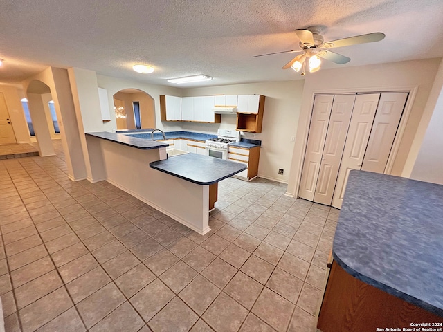 kitchen featuring white cabinets, kitchen peninsula, white gas range, and a textured ceiling