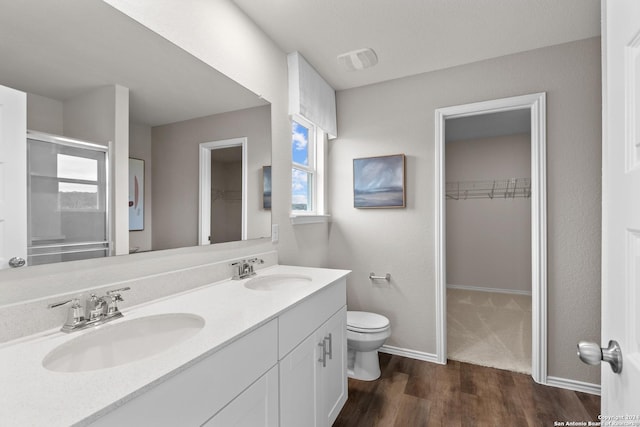 10411 Gibbons Crk, San Antonio, TX 78252 - bathroom featuring wood finished floors, toilet, double vanity, a walk in closet, and a stall shower