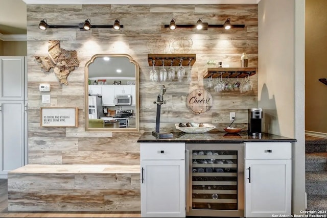 bar with ornamental molding, dark stone counters, appliances with stainless steel finishes, white cabinets, and beverage cooler