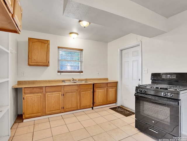 kitchen with light tile patterned floors, black gas range oven, and sink