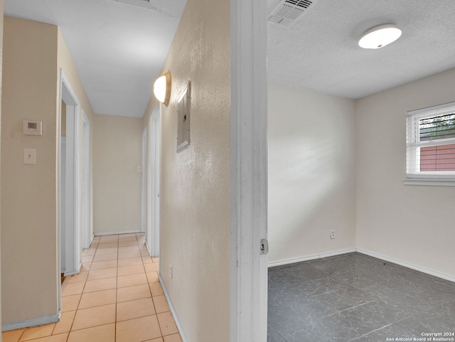 hallway with a textured ceiling, electric panel, and light tile patterned floors