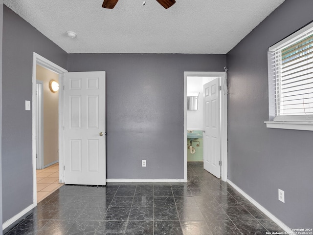 unfurnished bedroom featuring a textured ceiling, ensuite bath, and ceiling fan