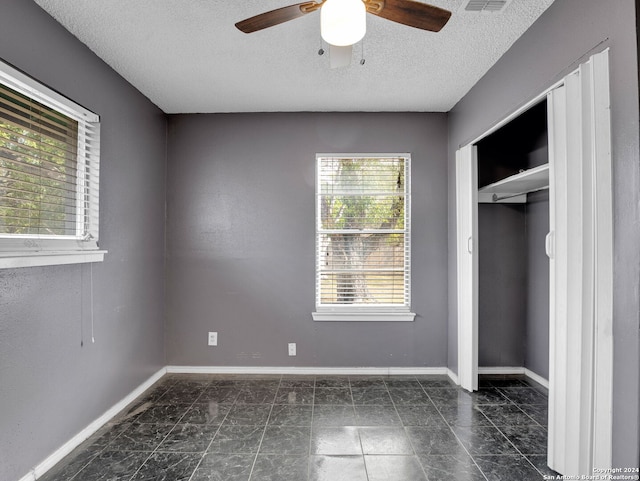 unfurnished bedroom featuring ceiling fan, multiple windows, a closet, and a textured ceiling