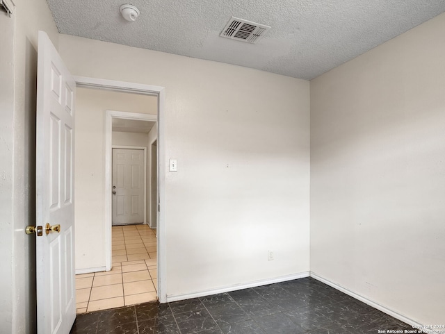 tiled empty room featuring a textured ceiling