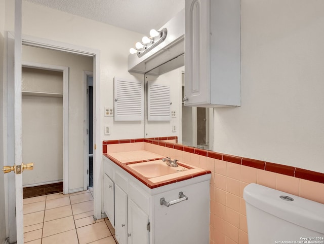 bathroom with tile walls, vanity, a textured ceiling, tile patterned flooring, and toilet