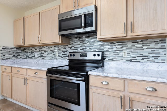 kitchen with tasteful backsplash, light brown cabinets, appliances with stainless steel finishes, and light stone countertops