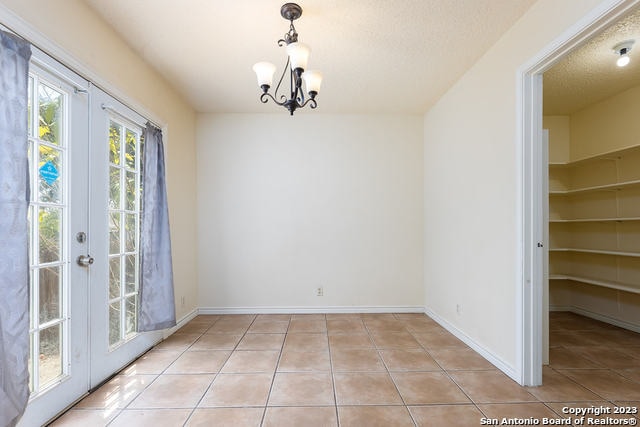 unfurnished dining area with an inviting chandelier, french doors, light tile patterned flooring, and a textured ceiling