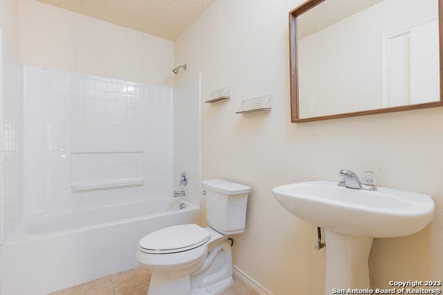 full bathroom with a textured ceiling, sink, tile patterned flooring, shower / washtub combination, and toilet