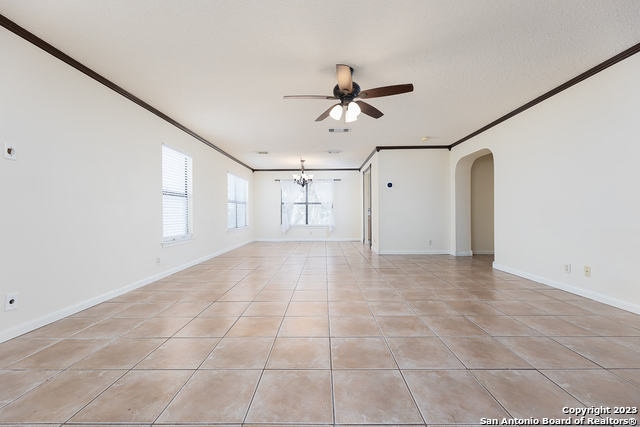 unfurnished room with ceiling fan with notable chandelier, light tile patterned floors, and crown molding