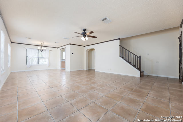 unfurnished living room featuring light tile patterned floors, ornamental molding, and ceiling fan with notable chandelier