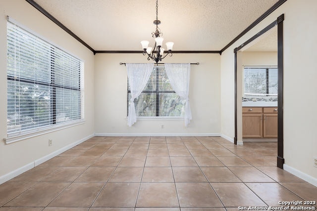 unfurnished dining area featuring crown molding, a textured ceiling, a chandelier, and light tile patterned floors