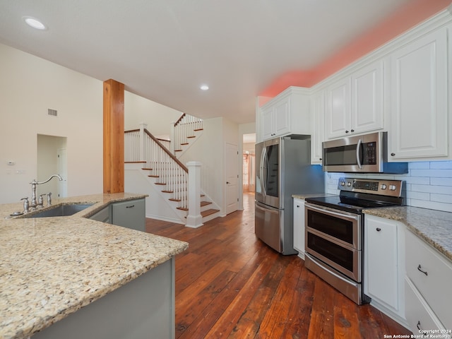 kitchen with sink, appliances with stainless steel finishes, light stone countertops, white cabinets, and dark hardwood / wood-style flooring