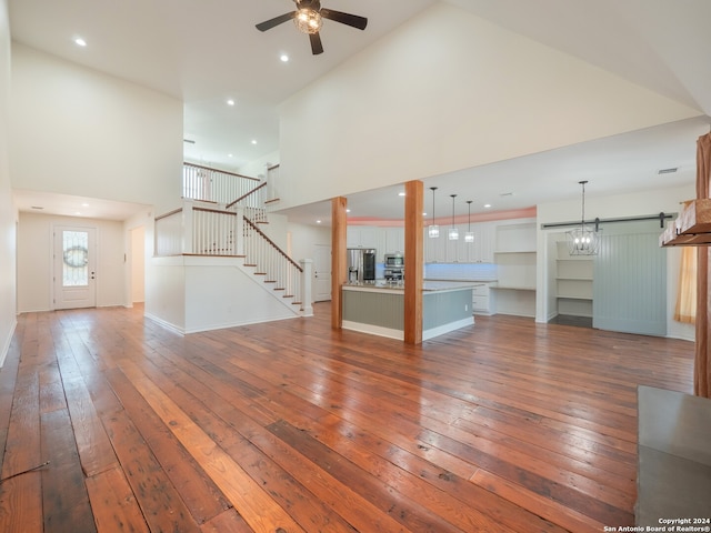 unfurnished living room with high vaulted ceiling, ceiling fan, a barn door, and dark hardwood / wood-style floors