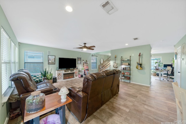 living room featuring a fireplace, a wealth of natural light, ceiling fan, and light hardwood / wood-style flooring