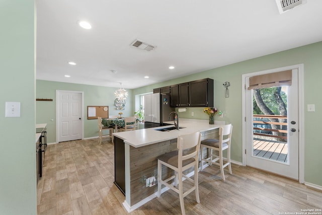 kitchen featuring sink, kitchen peninsula, a kitchen bar, dark brown cabinets, and light hardwood / wood-style flooring