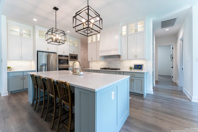 kitchen with stainless steel appliances, a center island with sink, white cabinets, and hardwood / wood-style floors